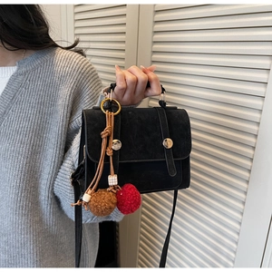 Dettaglio borsa nera scamosciata con cinghie decorative e ciondoli colorati in peluche