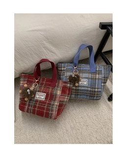 Detail of red and blue checkered woolen tote bags with plush charm on a soft carpet