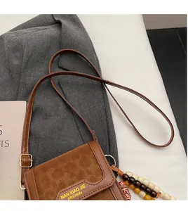 Detailed view of brown suede crossbody bag with colorful beaded tassel and logo
