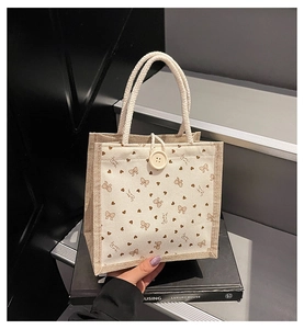 Détail du sac en lin avec motifs de nœuds bruns, bouton blanc et poignée en corde
