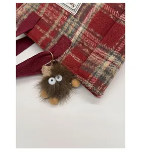 Detail of red-brown checkered wool tote bag with a cute brown plush monster charm