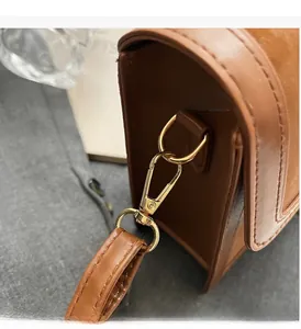 Detailed close-up of golden metal D-ring and lobster clasp on brown leather handbag