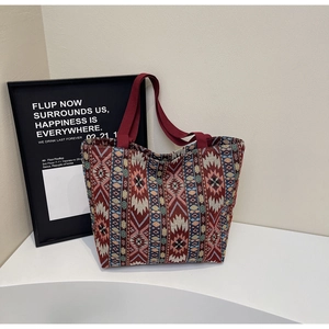 Détail du sac cabas tissé aux motifs géométriques et anses rouges sur support blanc