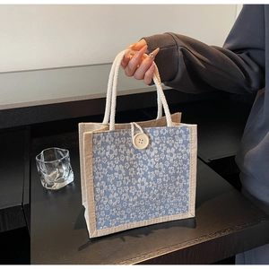 Detail of floral linen lunch bag showing woven rope handles and decorative wooden button