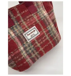 Macro detail of red plaid wool tote bag showing texture and stitched brand label