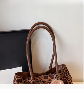 Detail of leopard print tote bag featuring brown leather handles and fuzzy charm accessory