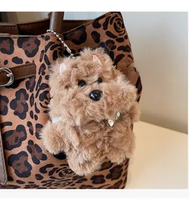 Detailed shot of brown plush puppy bag charm with TOP DOG bone tag on leopard print tote