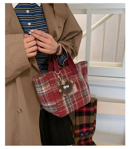 Detail of red and grey plaid tote bag with plush monster charm and woven straps