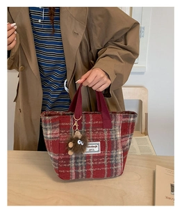 Detail of red plaid wool tote bag with white label and brown plush monster charm