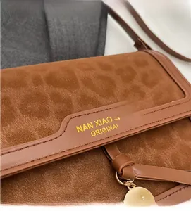 Vue détaillée du daim marron et du marquage doré sur ce sac à bandoulière vintage chic