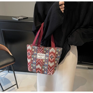 Detailed close-up of ethnic geometric jacquard tote bag with dark red canvas handles