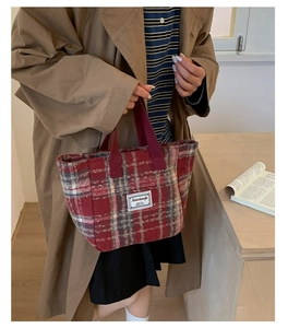 Detailed close-up of red plaid tweed tote bag with woven texture and white fabric patch