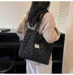 Detail of black tote bag with white bow pattern and brand patch in a home setting