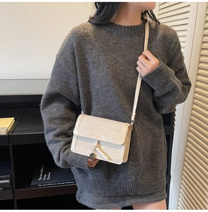 Détail du sac bandoulière crème avec motifs en relief et pendentif en métal doré