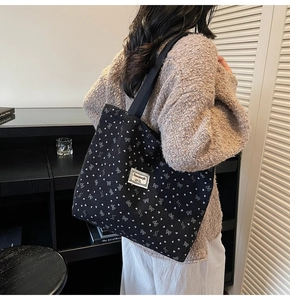 Close-up of black corduroy tote bag with silver bow patterns on a model's shoulder