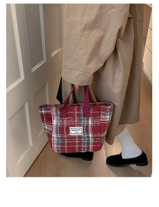 Detail of red plaid wool tote bag with textile handles and white rectangular brand label