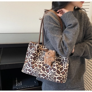 Detail of leopard print canvas tote bag featuring brown leather straps and plush bear charm