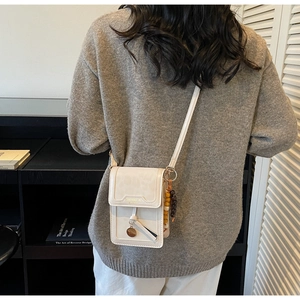 Chic beige crossbody phone bag with wooden bead charm shown on model in modern room