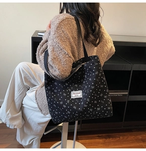Detail of black corduroy tote bag with white bow patterns and branded woven label