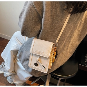 Detail of ivory flip crossbody bag featuring wooden bead charm and brand logo text