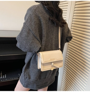 Détail du sac bandoulière en cuir blanc crème avec pompon et logo gaufré chic