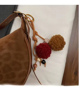 Gros plan du sac hobo en daim marron avec breloque en peluche rouge et perles de décoration