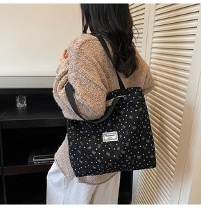 Detail of black canvas tote bag with white bow pattern worn by model for scale