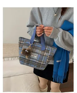 Detail of blue and brown plaid wool tote bag with blue handles and plush monster charm