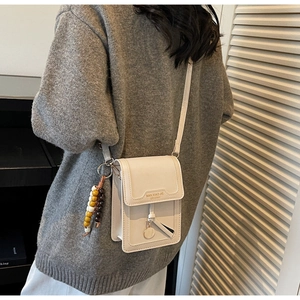 Close-up of cream crossbody phone bag with beaded charm and embossed logo detail