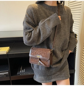 Détail du sac bandoulière léopard avec logo doré sur un pull en maille grise élégant