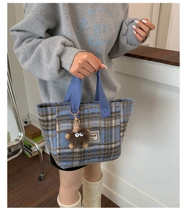 Detail of blue plaid woolen tote bag with letter label and cute plush monster charm