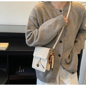 Detail of a beige crossbody phone bag with wooden beads on a model in a soft indoor setting