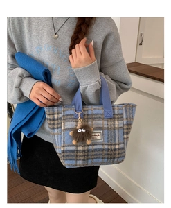 Detail of blue plaid tweed tote bag with a brown plush monster charm on the side