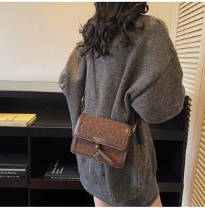 Détail du sac bandoulière léopard avec rabat et logo porté sur un pull gris foncé