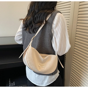 Détail du sac bandoulière beige minimaliste en forme de croissant avec étiquette