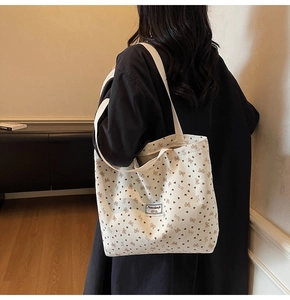 Detail of cream corduroy tote bag with bow patterns and branded woven label on shoulder