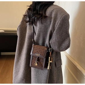 Detail of leopard print crossbody bag with wooden bead charm on a wool coat
