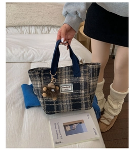 Detail of wool blend plaid tote bag with teddy bear charm in autumn home setting