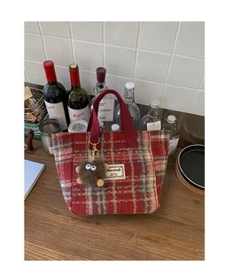 Detail of red plaid tweed tote bag featuring a cute plush monster charm and brand tag