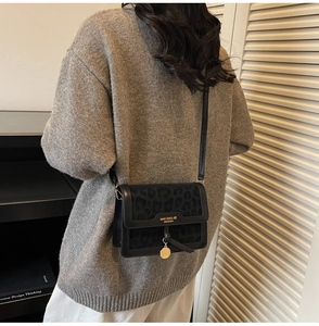 Gros plan du sac bandoulière noir à motif léopard avec logo doré et pendentif rond