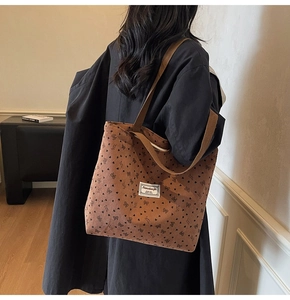 Detail of brown corduroy tote bag with black heart patterns and branded fabric label