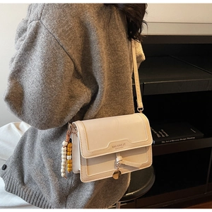 Détail d'un sac bandoulière blanc crème avec gland à franges et ornements métalliques