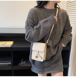 Detail of a minimalist cream crossbody phone bag with metal pendant and tassel accent