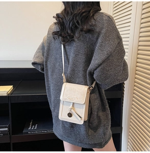 Close-up of a cream leather crossbody phone bag with flap closure and metal pendant