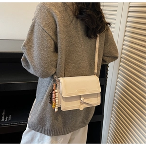 Détail du sac à bandoulière en cuir PU blanc cassé avec pendentif en perles et nœud décoratif