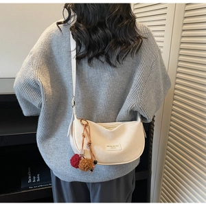 Détail du sac demi-lune beige en cuir avec un pendentif décoratif en forme de pompon