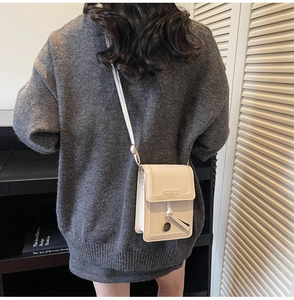 Detail of cream white leather crossbody bag with metal pendant and brand embossed flap