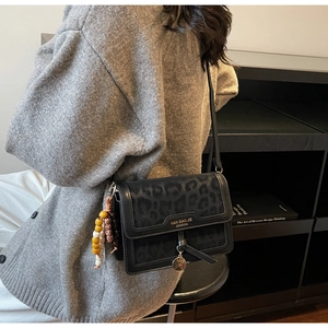 Détail d'un sac bandoulière noir embossé léopard avec breloque perlée et logo en métal