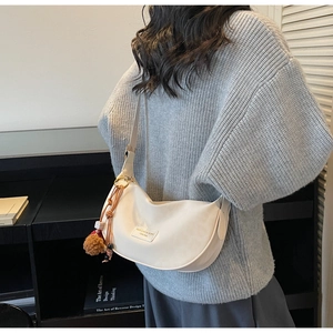 Détail du sac demi-lune blanc cassé en tissu texturé avec pendentif boule de poils