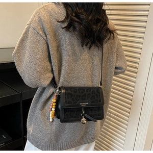 Détail du sac bandoulière noir à motif léopard avec perles en bois et breloque en métal